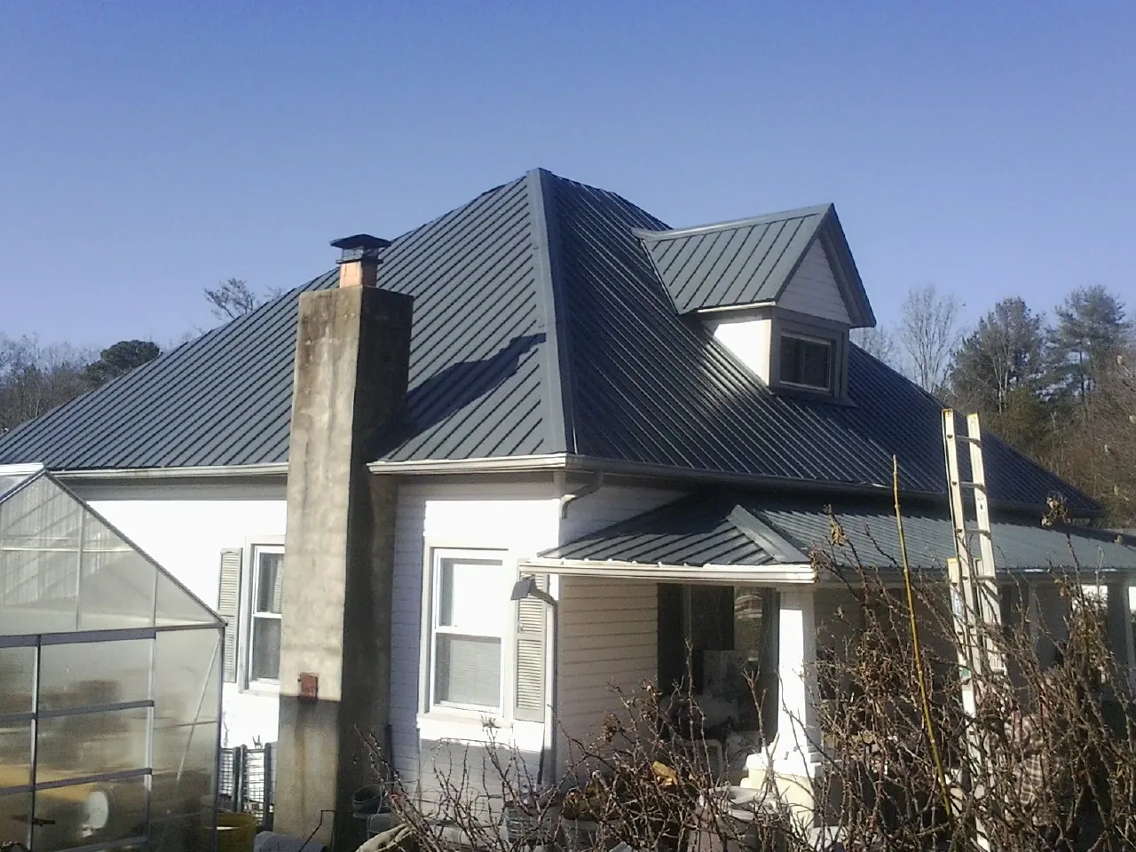 Dark blue standing seam metal roof on a white farmhouse with dormer — Slate & Tile Roof Repair by Roofing Brothers in Mico
