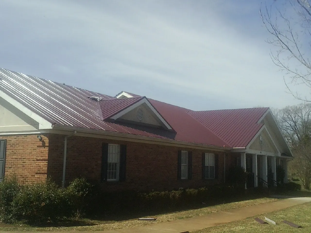 Red metal roof with gabled entries on a long brick building, from a Hail Damage Roof Repair job in Mico