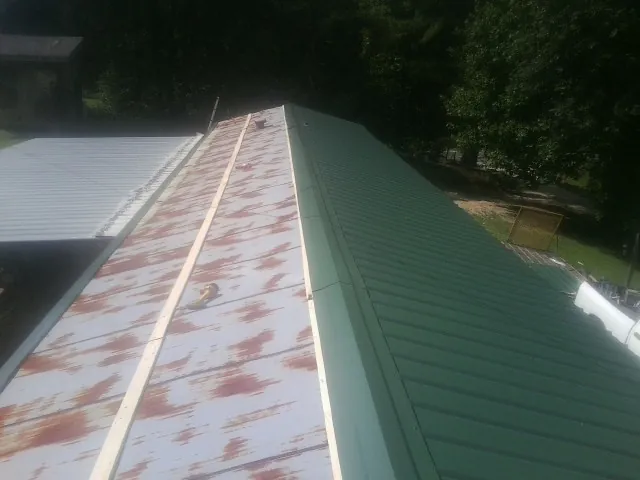 Old rusted panels beside newly installed green metal roofing — Wind Damage Roof Repair by Roofing Brothers in Mico