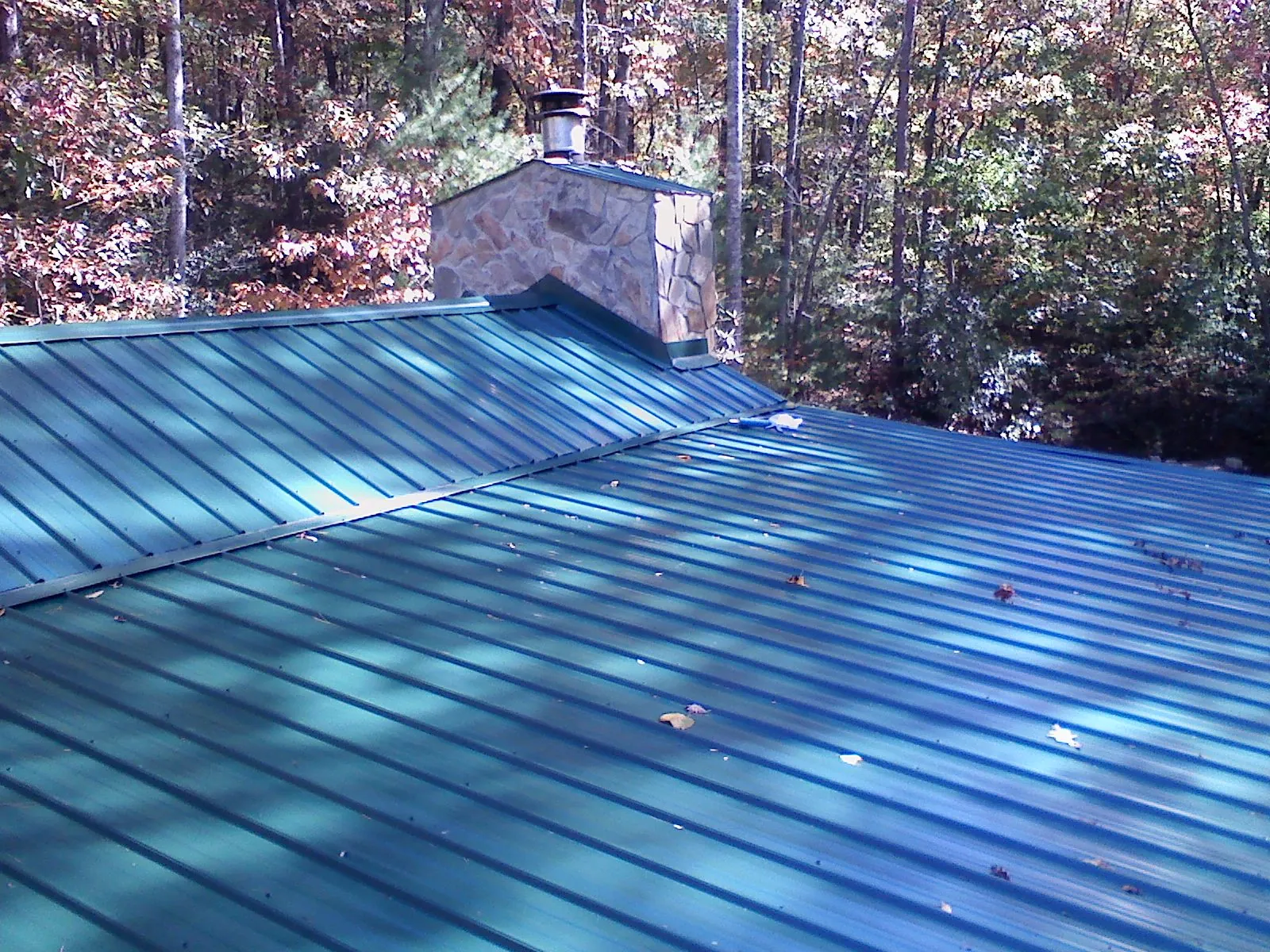New green metal roof and stone chimney surrounded by autumn woods in Mico